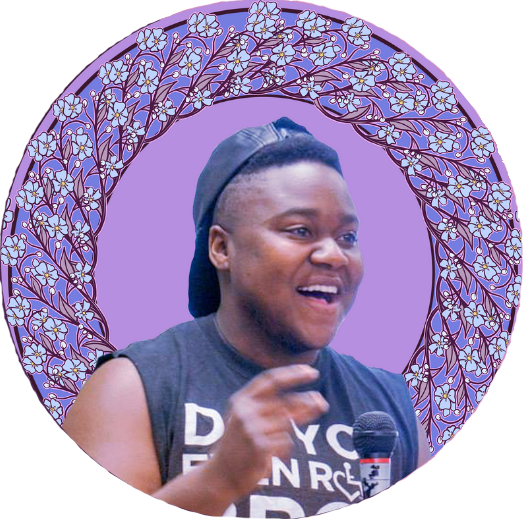 Ki'tay smiling while speaking with a microphone, surrounded by a drawn wreath of woven blue flowers on a purple field